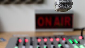 Photo of an on air radio station sign and broadcast board.